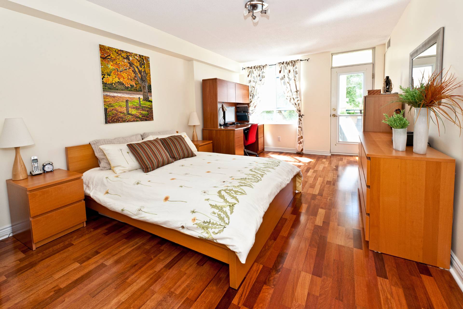 Water Damage Mitigation Services 18 A new bedroom in a cozy home features a wooden bed frame, white and green bedding, two bedside tables with lamps, a desk, a dresser, a wall painting, a large window, and wooden floors.