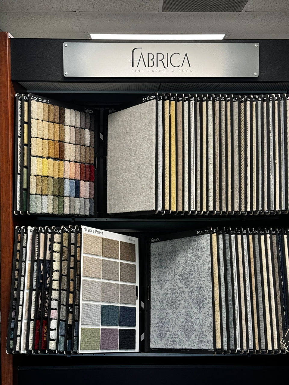About 5 Display of various fabric swatches arranged in two rows under a sign that reads "Fabrica Fine Carpet & Rugs".