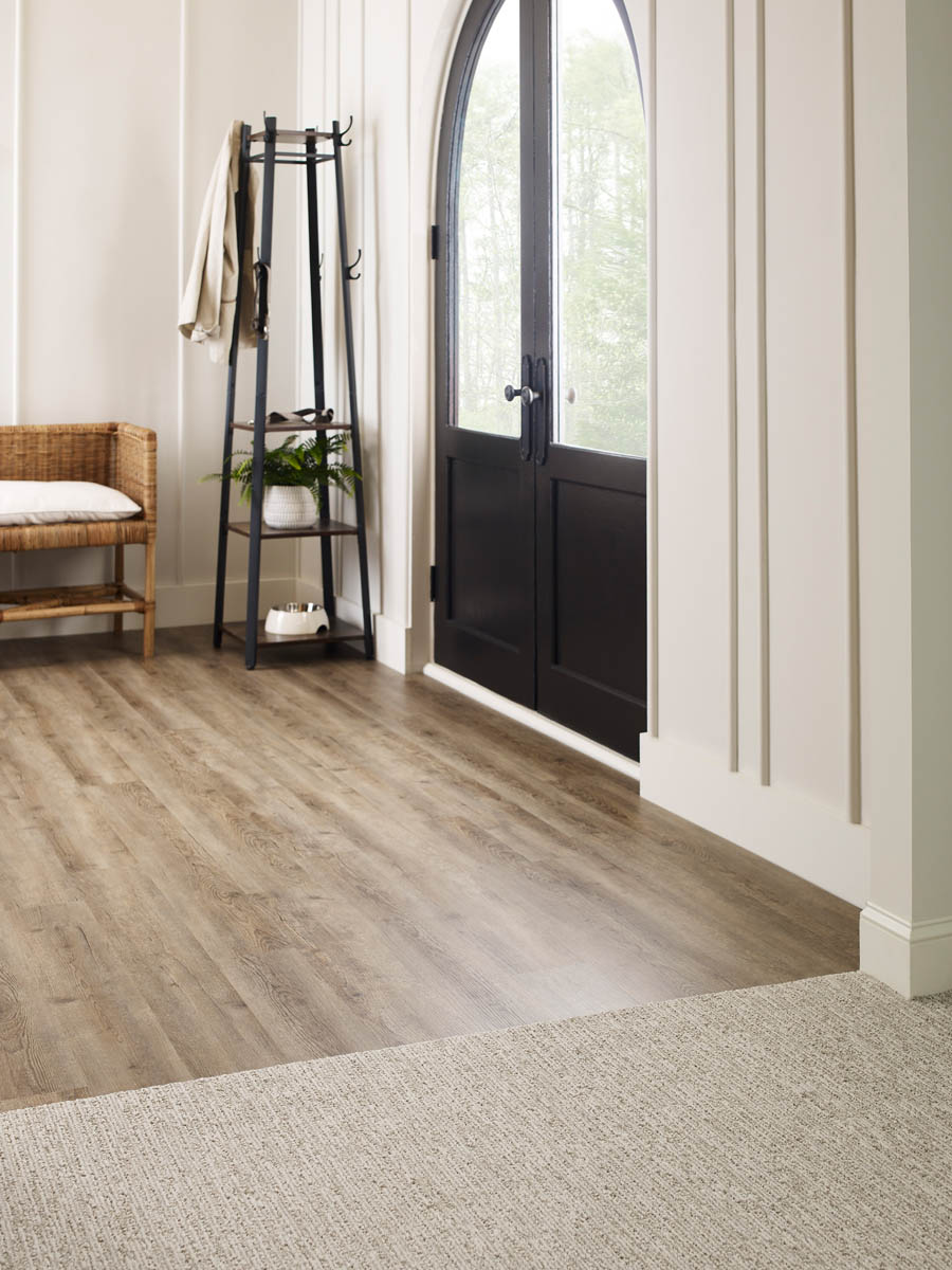 Flooring Installation 11 A minimalistic entryway featuring a wooden bench, black stand with coat and bag, wood and carpet flooring, and a black arched door with windows.