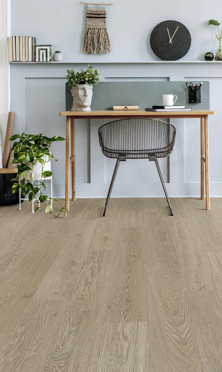 Flooring Installation 6 A minimalist home office features a wooden desk with decor and a chair, against a light gray wall with paneling. A plant and other decorative items are visible on the floor and desk.