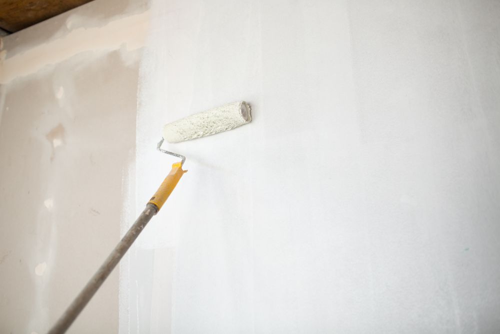 Painting And Drywall Repair 6 A paint roller with an extended handle is being used to efficiently tackle painting and drywall repair on a white wall.