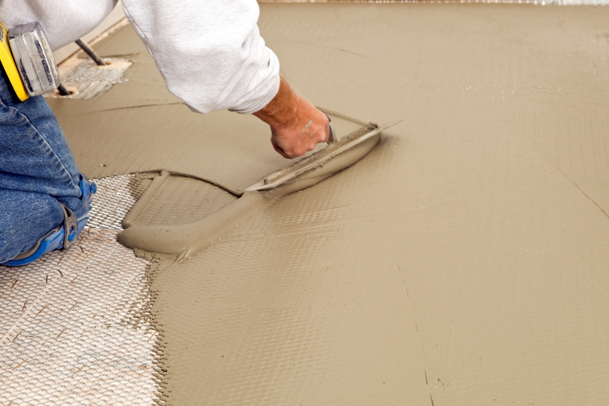 Blog 4 A person smooths wet concrete with a trowel on a construction site, laying the foundation for a new bathroom subfloor.