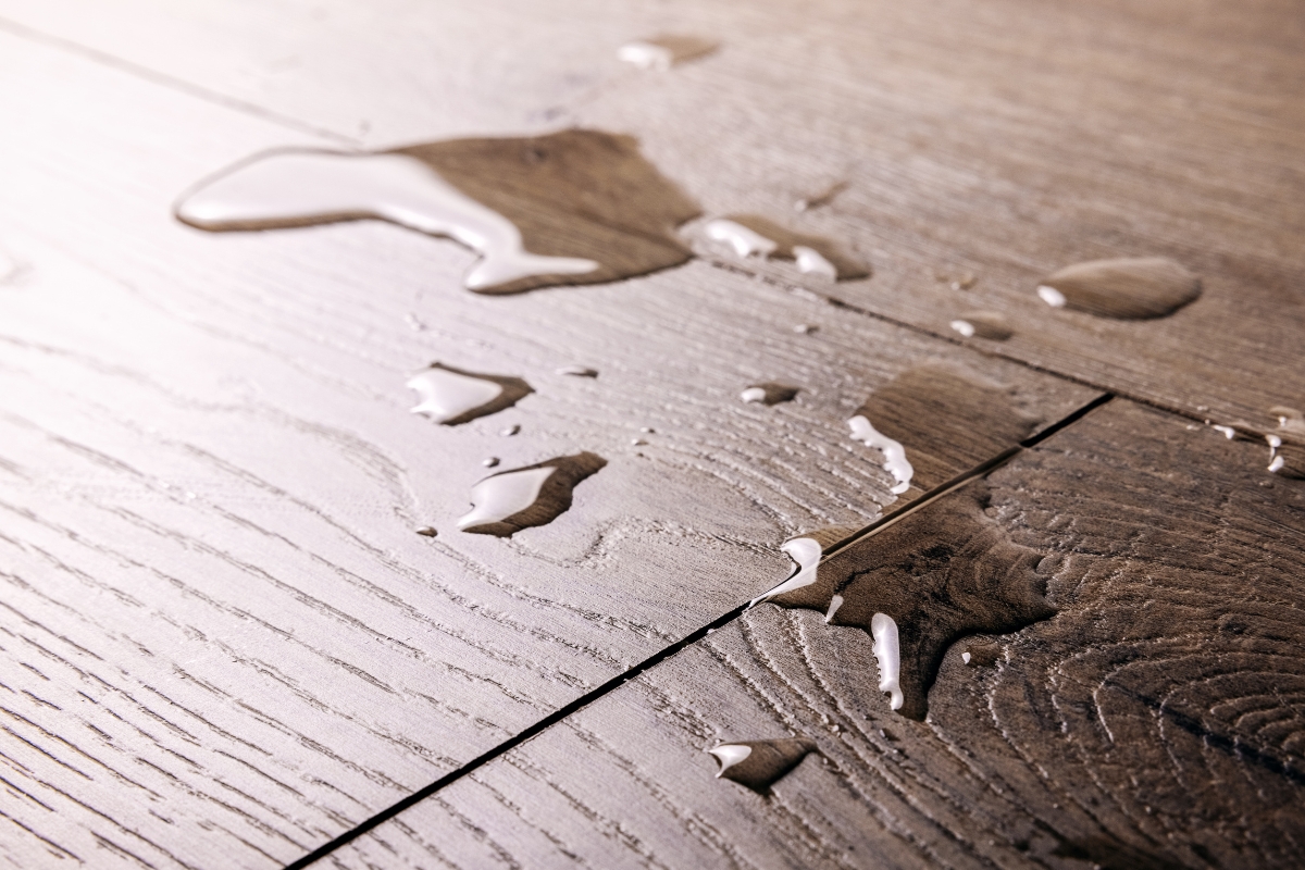Vinyl Vs Laminate Flooring: Which Is Best For Your Georgia Home? 4 Water spills across a wooden floor with visible grain patterns, reminiscent of laminate flooring often found in cozy Georgia homes.