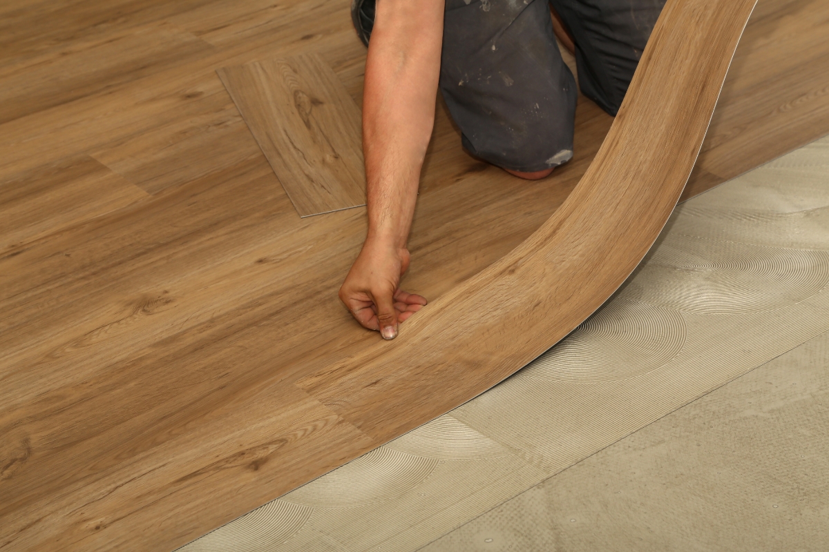 Vinyl Vs Laminate Flooring: Which Is Best For Your Georgia Home? 14 In a cozy Georgia home, a person meticulously installs vinyl plank flooring, carefully pressing down the edges with their hand to ensure a seamless finish.