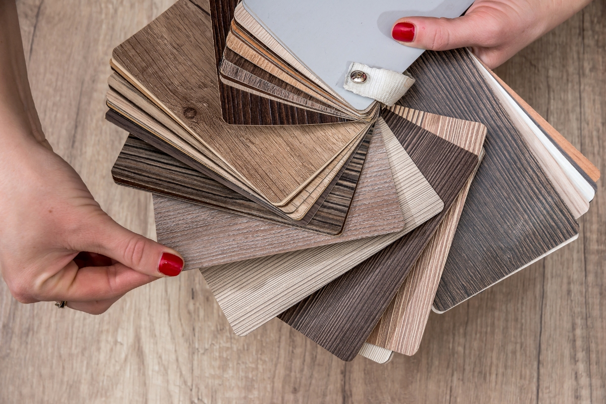 Vinyl Vs Laminate Flooring: Which Is Best For Your Georgia Home? 15 Hands holding a fan of wood laminate samples in various shades and textures, perfect for choosing new laminate flooring for your Georgia home, spread across a wooden surface.