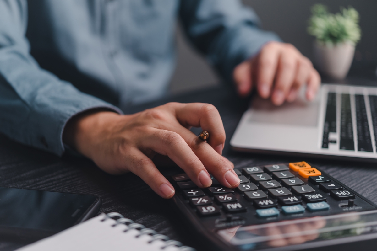 Vinyl Vs Laminate Flooring: Which Is Best For Your Georgia Home? 3 A person is working diligently at a laptop and calculator, surrounded by a notepad and smartphone on a dark table, reflecting the sleek aesthetic of their Georgia home's laminate flooring.