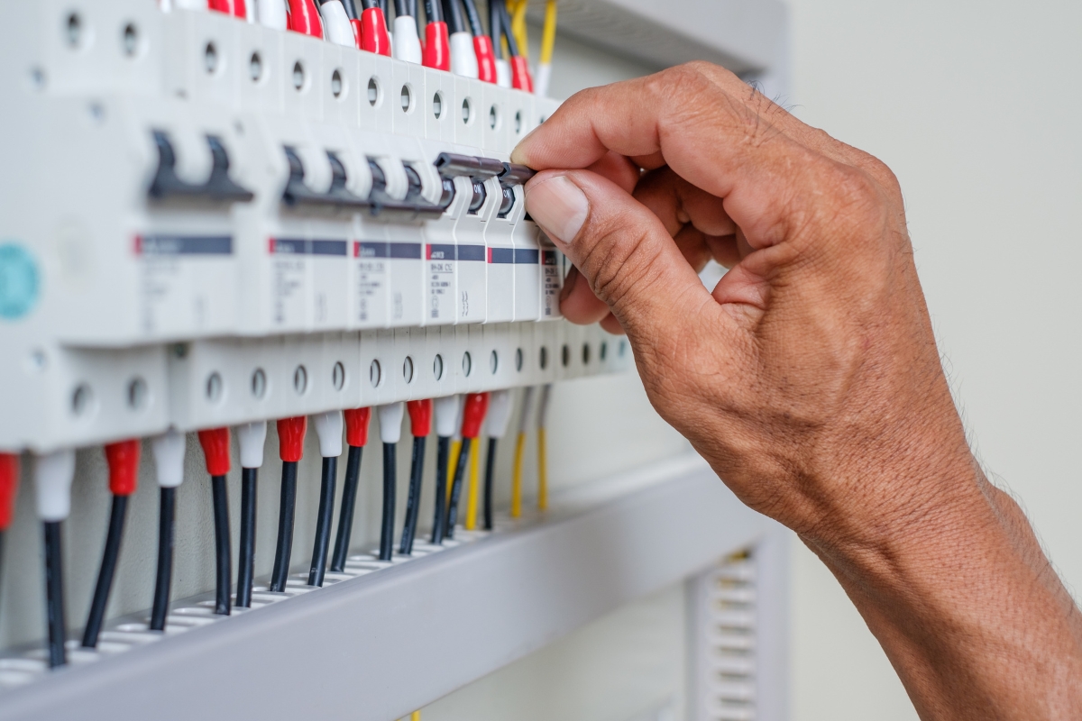 Fire Damage Restoration: Transform Your Home Back To Normal Swiftly 2 A person’s hand switches a circuit breaker on an electrical panel with multiple wires and switches, a crucial step in fire damage restoration to ensure safety before repairs begin.