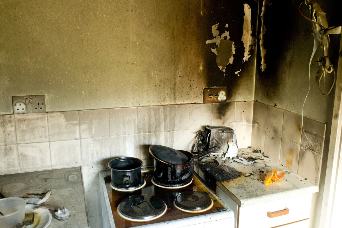 Fire Damage Restoration: Transform Your Home Back To Normal Swiftly 3 A kitchen with scorched walls, burnt pots on the stove, and visible fire damage on the countertop and backsplash in need of professional Fire Damage Restoration.