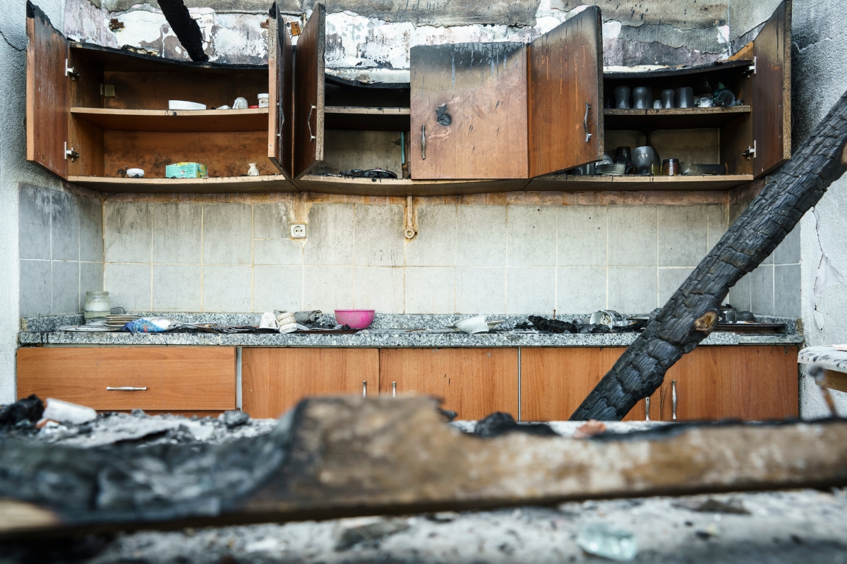 Fire Damage Restoration: Transform Your Home Back To Normal Swiftly 5 A kitchen with burnt cabinets, soot-covered surfaces, charred debris, and partially open cupboards shows the need for Fire Damage Restoration after a fire.