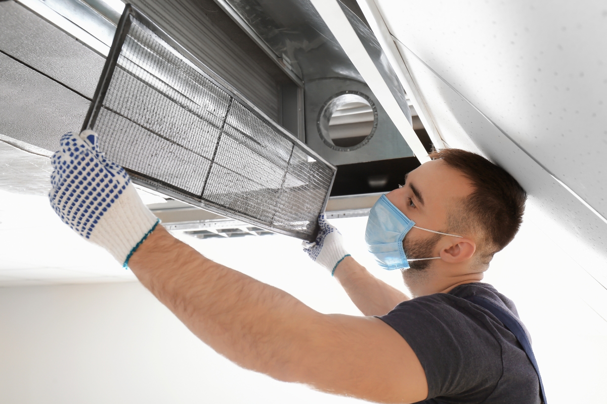 Fire Damage Restoration: Transform Your Home Back To Normal Swiftly 6 A man wearing gloves and a face mask is removing an air filter from a ceiling ventilation duct as part of fire damage restoration.
