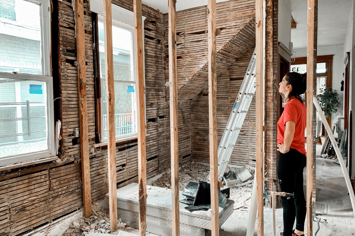 Fire Damage Restoration: Transform Your Home Back To Normal Swiftly 7 A person in a red shirt stands in a partially demolished room with exposed wooden studs, surveying the area during fire damage restoration.
