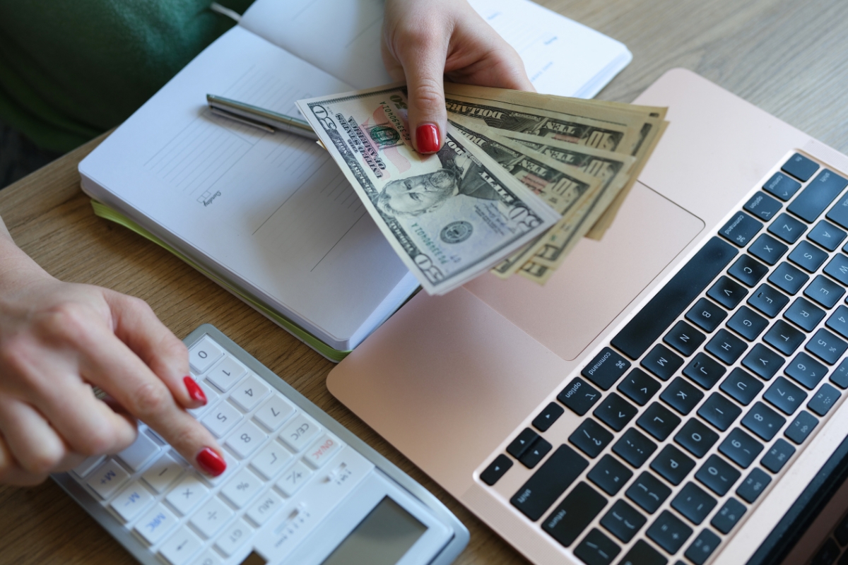 Kitchen Remodeling In Atlanta: How To Transform Your Space 2 A person counts US dollar bills while using a calculator, with a notebook and a laptop on the desk, planning their kitchen remodeling budget.