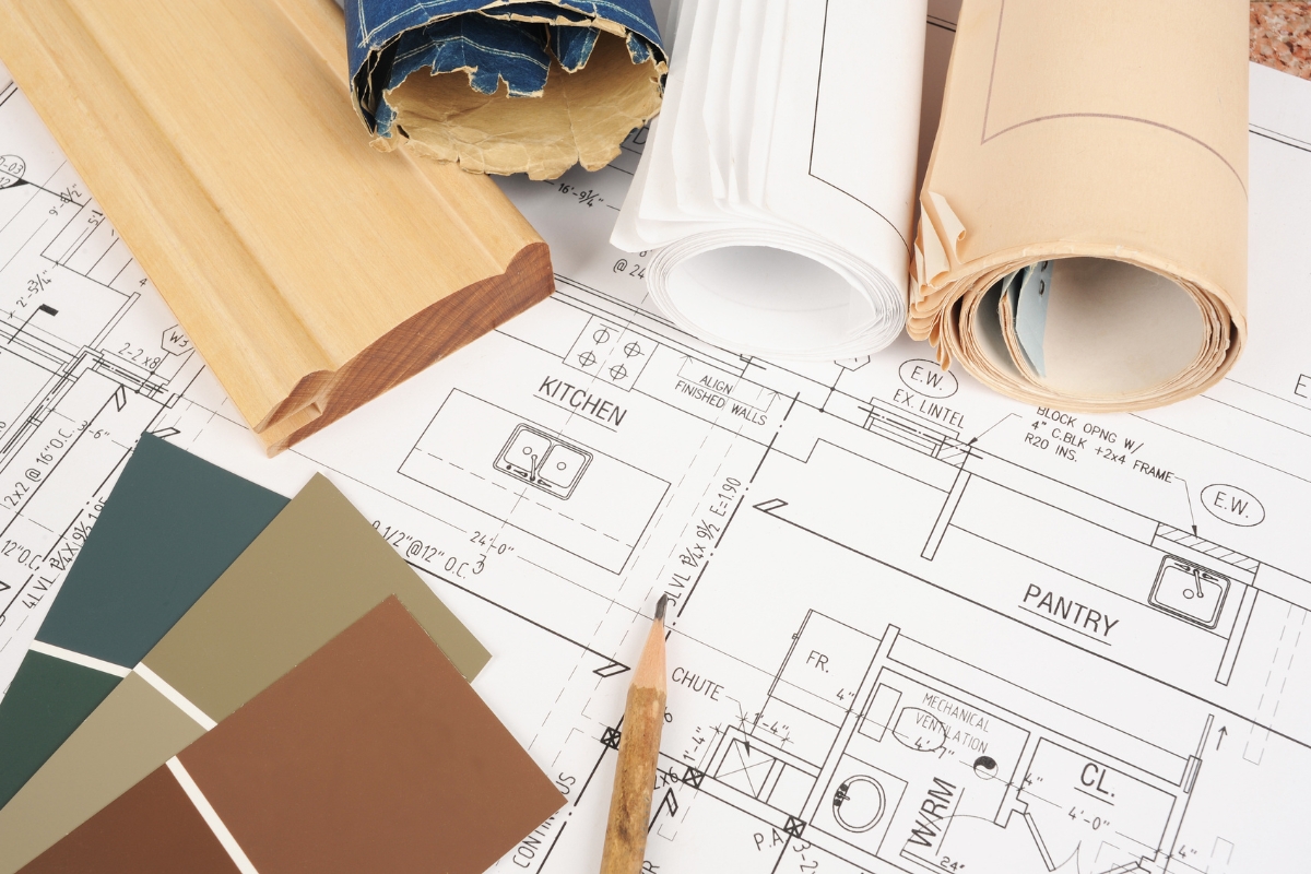 Kitchen Remodeling In Atlanta: How To Transform Your Space 3 Architectural blueprints, wood trim samples, paint color swatches, and rolled plans arranged on a table, illustrating home design and kitchen remodeling planning.