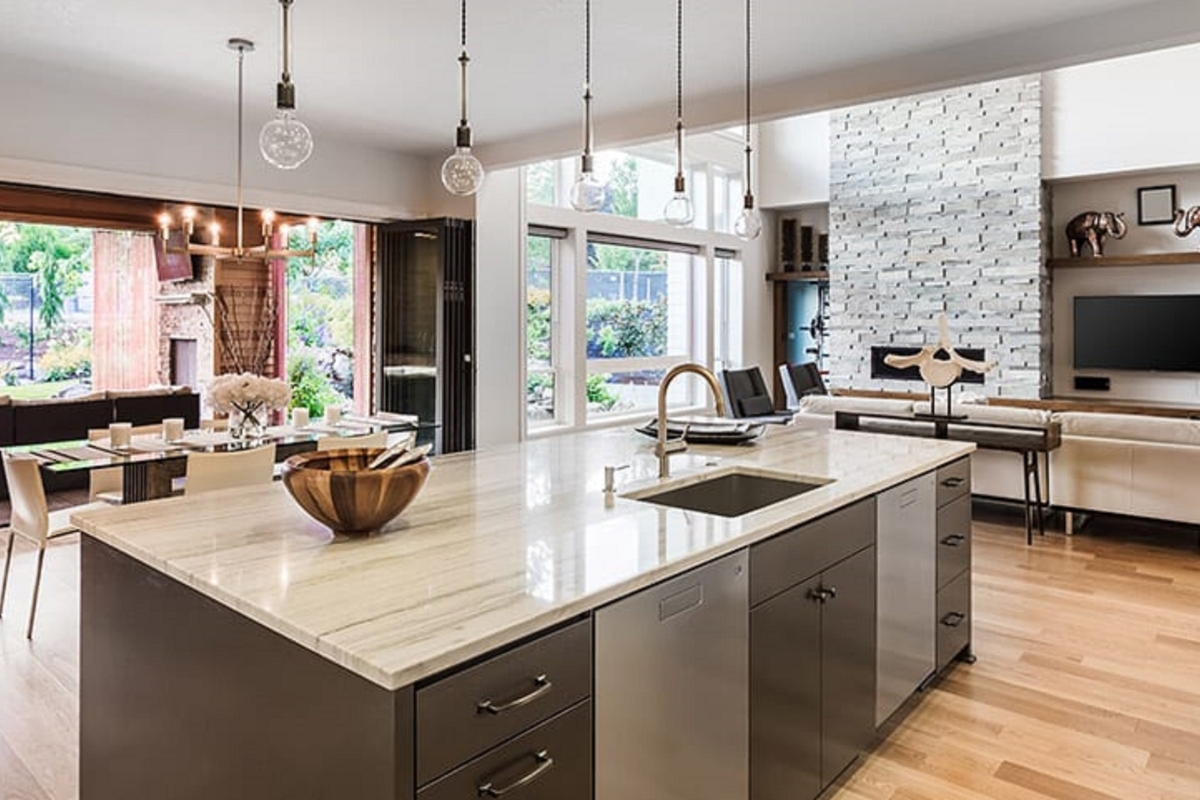 Kitchen Remodeling In Atlanta: How To Transform Your Space 1 Modern open-plan kitchen and living area with a marble island, stainless steel appliances, wood floors, and large windows overlooking a garden—perfect for your next kitchen remodeling inspiration.