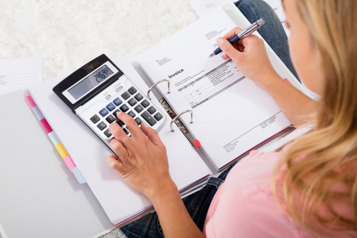 Luxury Vinyl Plank Flooring: Transform Modern Homes With Style And Durability 5 A person uses a calculator and writes on an invoice in a binder, sitting with organized folders and documents on a desk featuring sleek vinyl plank flooring.