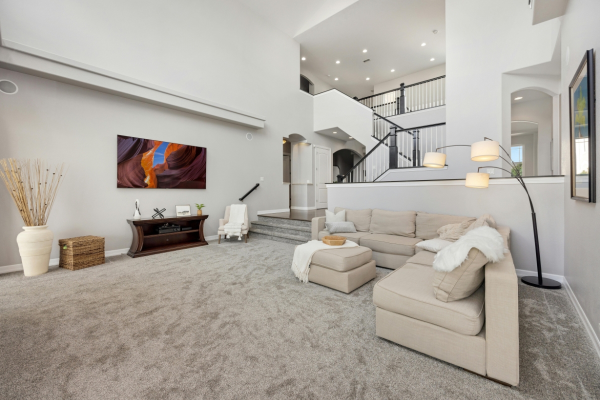 Carpet Replacement: Top Signs It’s Time For A New Carpet In Your Home 5 Spacious living room with a beige sectional sofa, ottoman, floor lamp, TV on a stand, gray carpet ready for carpet replacement, and an open staircase leading to the upper level.