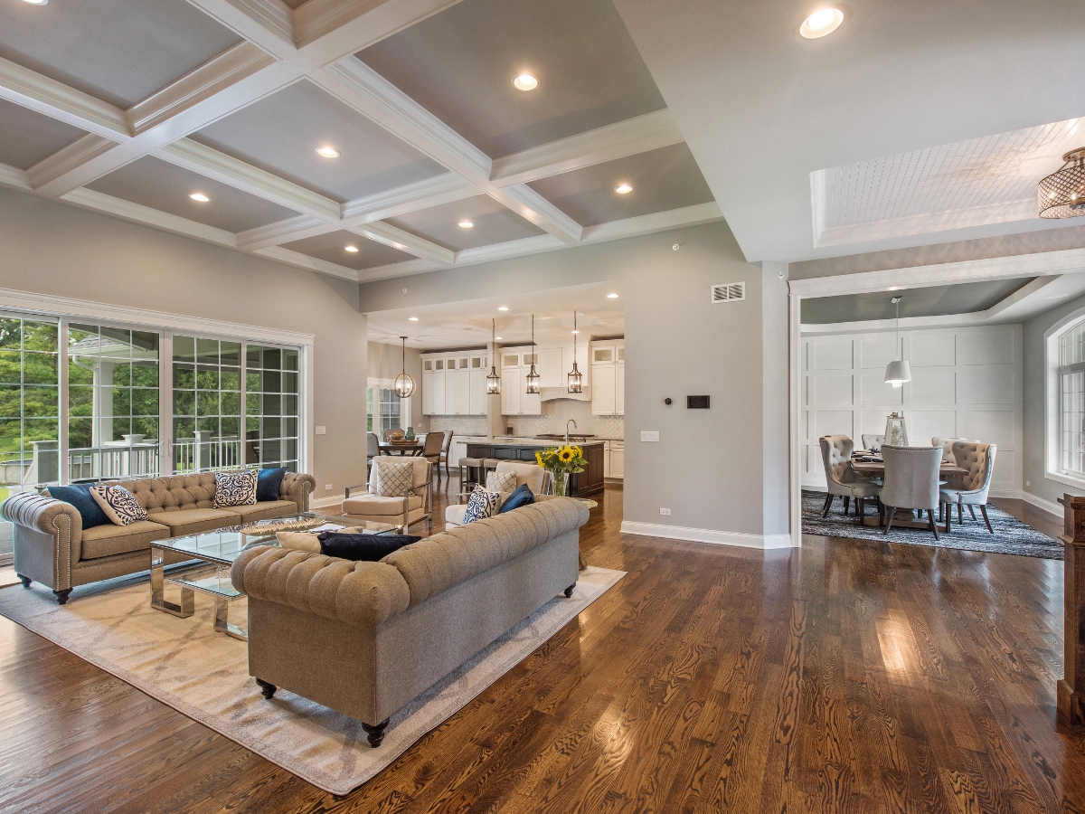 Best Flooring For High-Traffic Areas: A Homeowner’s Guide To Durability And Style 10 Open-concept living area with coffered ceiling, best flooring for high-traffic areas, two sofas, kitchen in the background, and a dining room with a large window to the right.