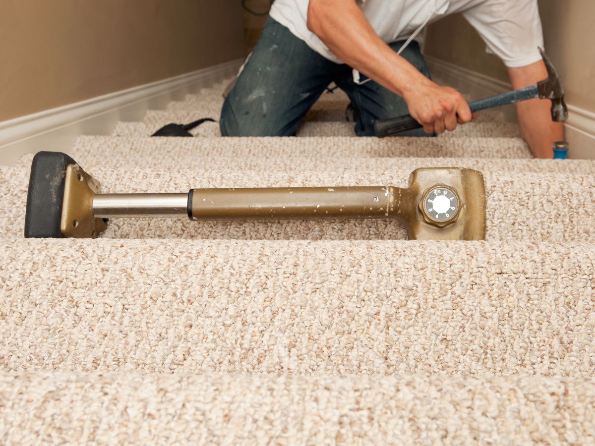 How Professional Carpet Stretching Can Extend The Life Of Your Floors 1 A professional carpet installer demonstrates expert technique with a knee kicker tool, using one hand to adjust the carpet and the other to hold a hammer—showcasing skills in professional carpet stretching on stairs.