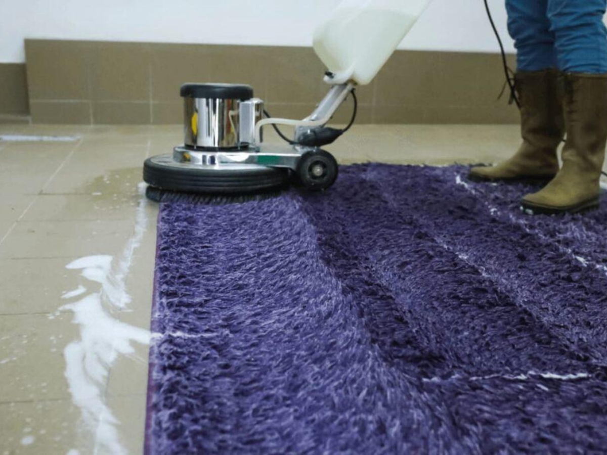 How Professional Carpet Stretching Can Extend The Life Of Your Floors 3 A person uses a floor cleaning machine with soap to clean a purple shaggy carpet on a tiled floor, ensuring the surface is spotless before any Professional Carpet Stretching service.