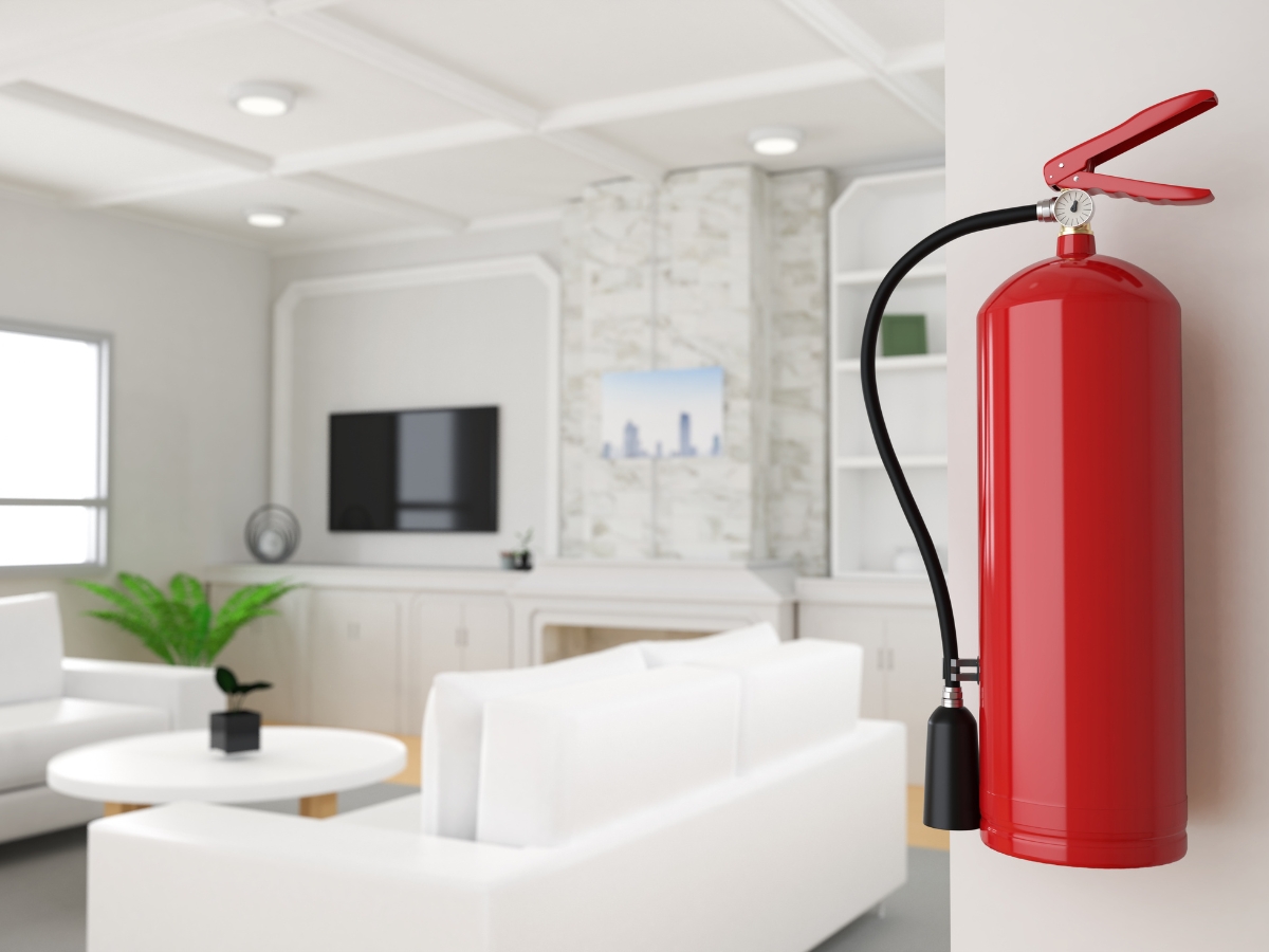 Fire Prevention Tips To Protect Your Home And Family This Fall 2 A red fire extinguisher is mounted on a white wall in a modern living room with white furniture and a TV, serving as a practical reminder of essential Fire Prevention Tips.