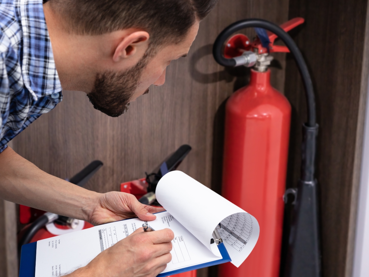 Fire Prevention Tips To Protect Your Home And Family This Fall 3 A person inspecting fire extinguishers and recording information on a clipboard, demonstrating essential fire prevention tips.
