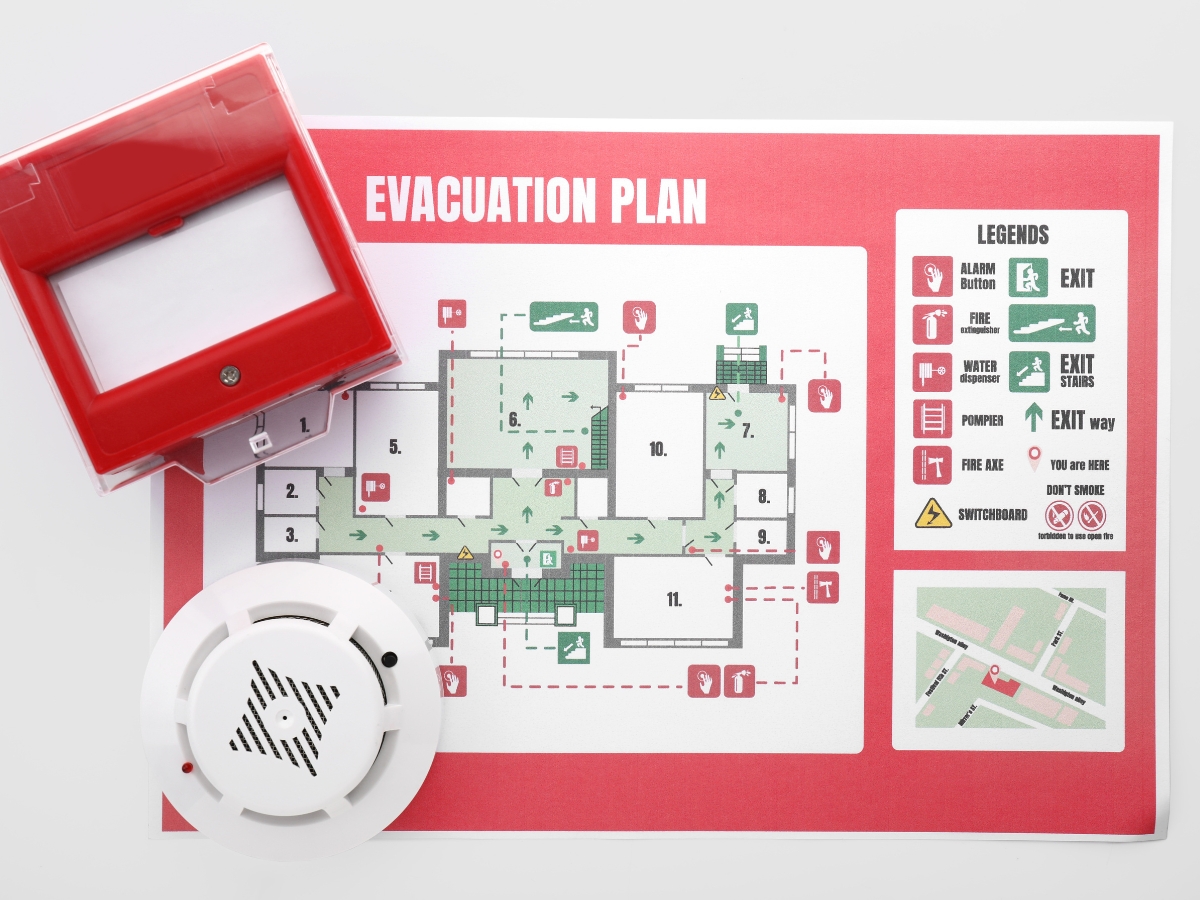 Fire Prevention Tips To Protect Your Home And Family This Fall 5 A fire alarm device and smoke detector placed on a printed evacuation plan with labeled exits and legend symbols, highlighting essential Fire Prevention Tips for enhanced safety awareness.