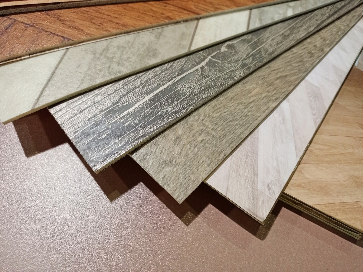Hardwood Vs. Engineered Wood Flooring: Which One Is Right For You? 5 Several vinyl flooring samples in various wood and stone patterns are fanned out on a flat surface, offering stylish alternatives to traditional options like Hardwood vs. Engineered Wood Flooring.