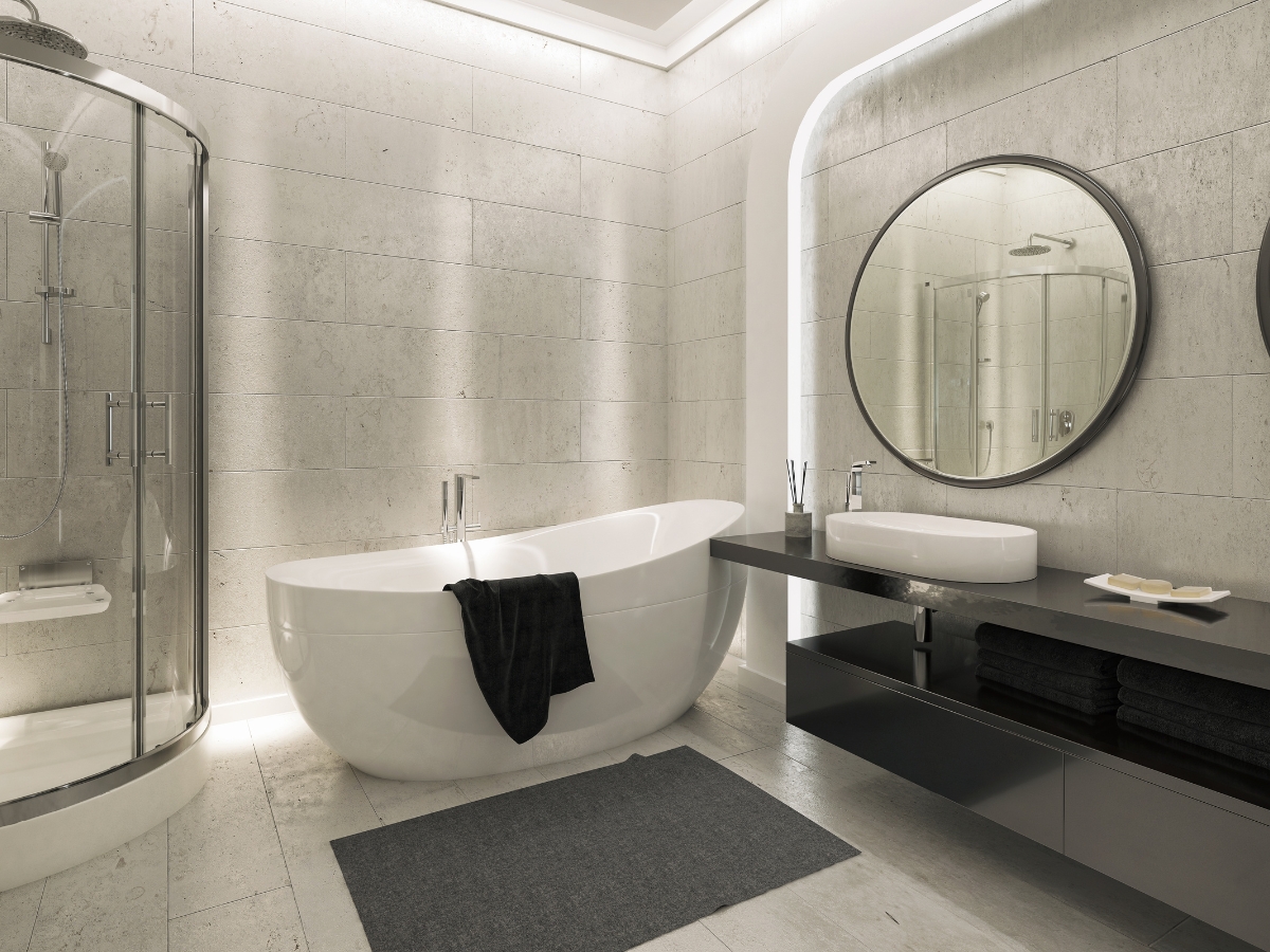 Modern bathroom featuring a freestanding bathtub, wall-mounted sink, round mirror, and glass shower enclosure—showcasing Bathroom Remodeling Trends for 2025 with minimal decor in soothing neutral tones.