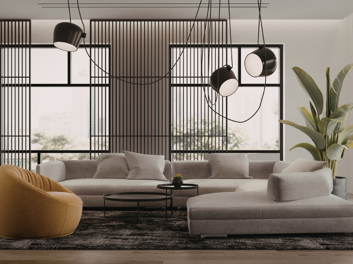 Modern living room with a gray sectional sofa, round black coffee tables, a mustard yellow chair, large windows, hanging lights, and a tall green plant that enhances the space’s biophilic design.