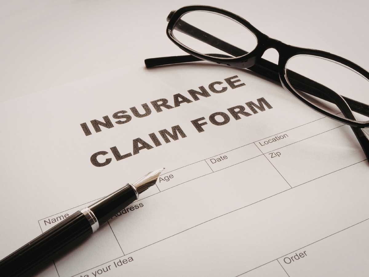 A pen and eyeglasses rest on top of an insurance claim form for fire damage recovery, partially filled out with sections for name, age, date, location, and zip code.