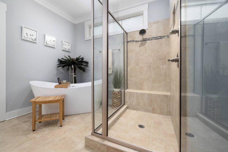 Modern bathroom featuring a glass-enclosed shower, freestanding bathtub, small wooden stool, potted plant, and framed wall art—perfect inspiration for your next shower remodeling or bathroom remodeling project.