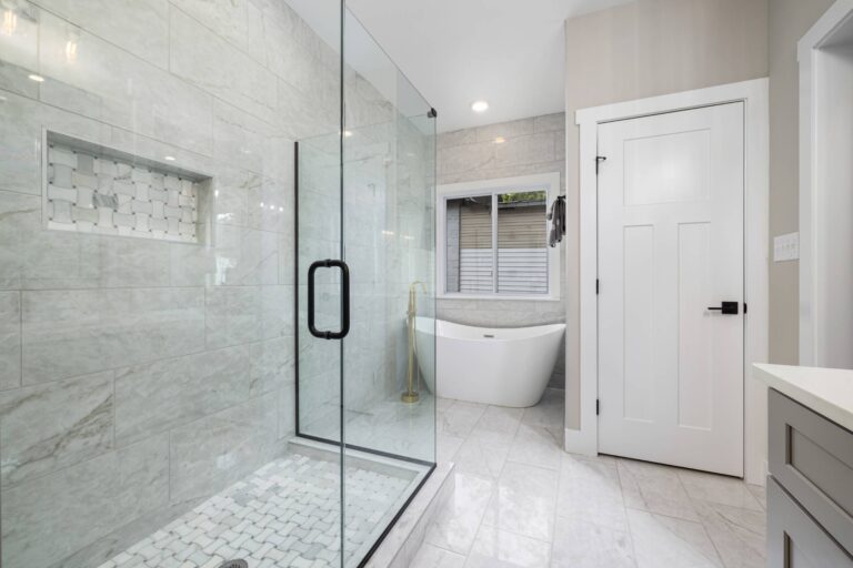 Bathroom And Shower Remodeling 5 Bathroom and Shower Remodeling featuring a modern glass-enclosed shower, white freestanding bathtub, large window, and light-colored tile flooring and walls.