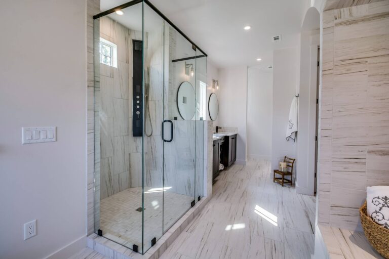 Bathroom And Shower Remodeling 8 Modern bathroom with a glass walk-in shower, dual sinks with round mirrors, marble-style tile flooring, and a wicker laundry basket—ideal inspiration for your next bathroom remodeling project.