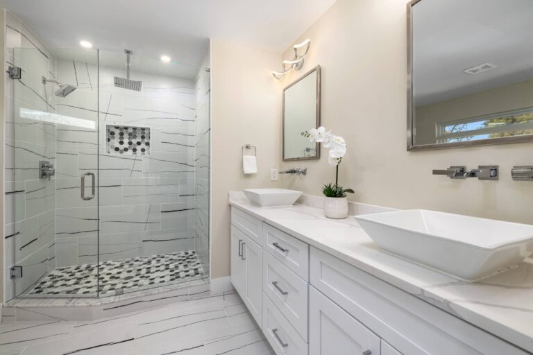 Bathroom And Shower Remodeling 7 Modern bathroom with a glass-enclosed shower, double sinks with vessel basins, white cabinetry, wall-mounted faucets, and a potted orchid—perfect inspiration for your next bathroom remodeling project.