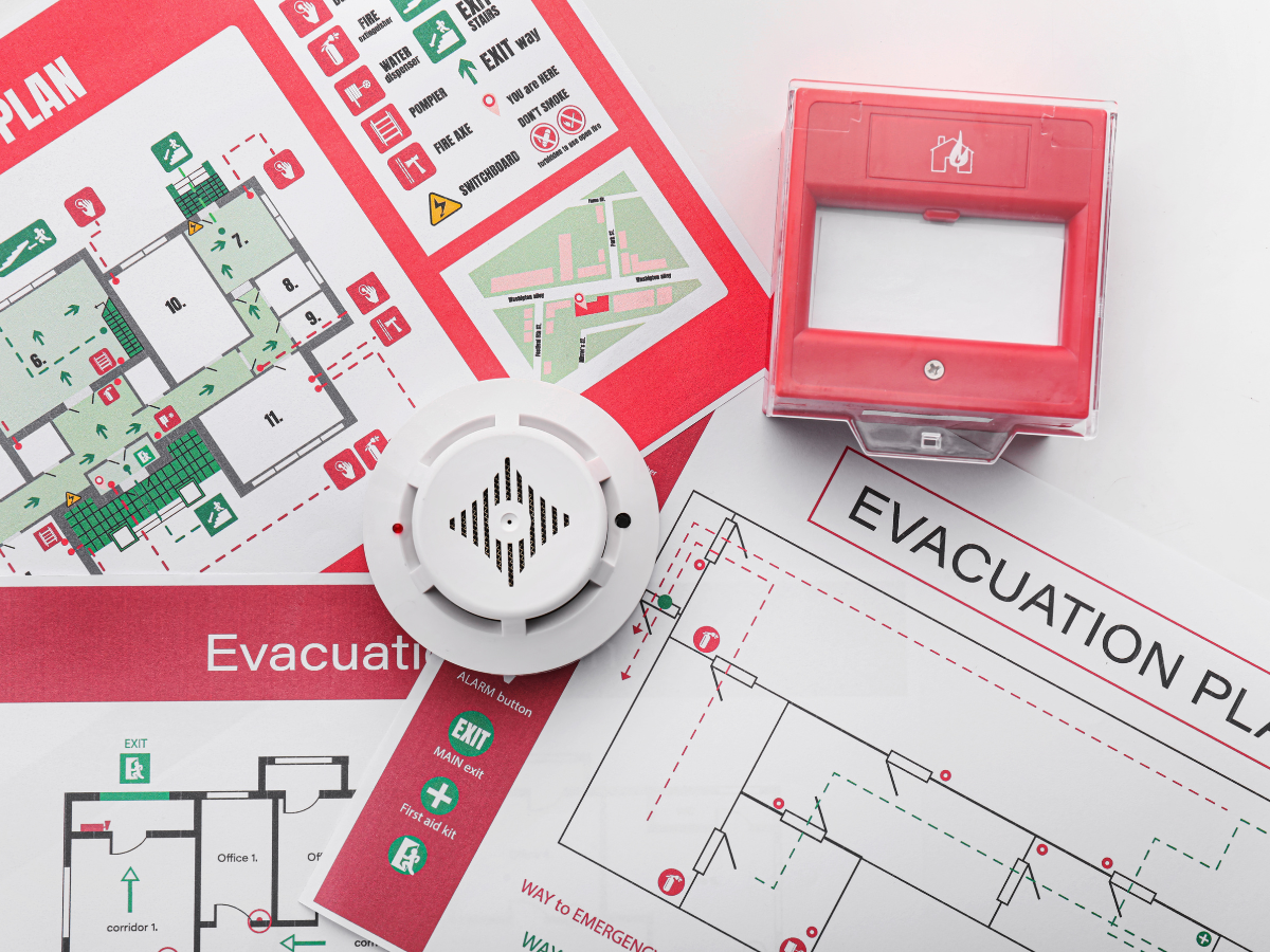 Storm Prep For Atlanta Homes: Emergency Tips And Recovery Strategies 1 Fire evacuation plans, a smoke detector, and a red fire alarm box are displayed on a white surface, illustrating emergency preparedness materials for both fire safety and storm prep.