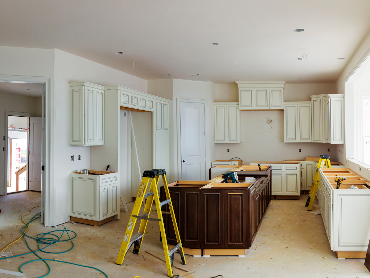 A kitchen under construction with ladders, cabinets being installed, tools on the island, and unfinished floors reflects the meticulous attention to detail found in basement remodeling Atlanta projects.