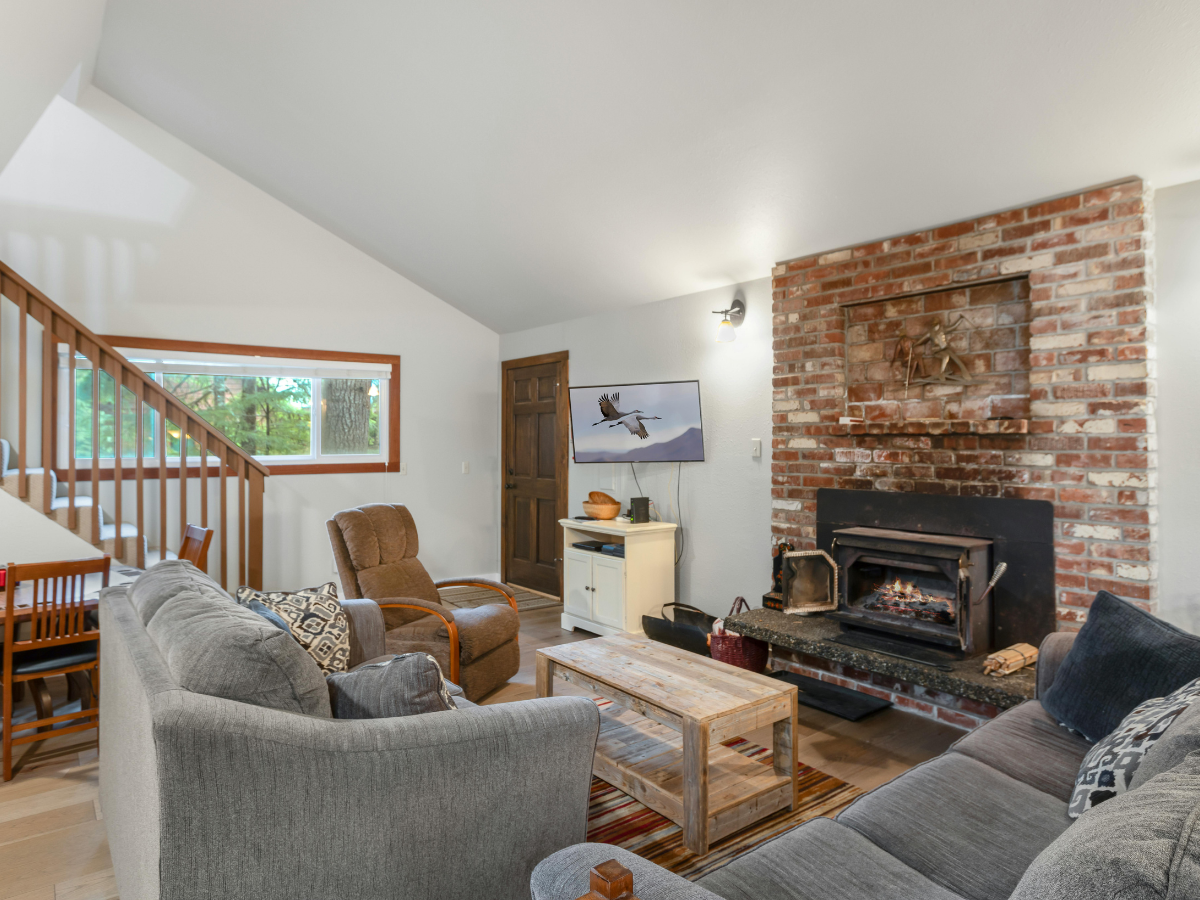 Cozy living room with a gray sofa, wooden coffee table, brick fireplace, TV, and stairs leading up&mdash;perfect inspiration for basement remodeling Atlanta style. A window and wooden accents add warmth to this inviting space.
