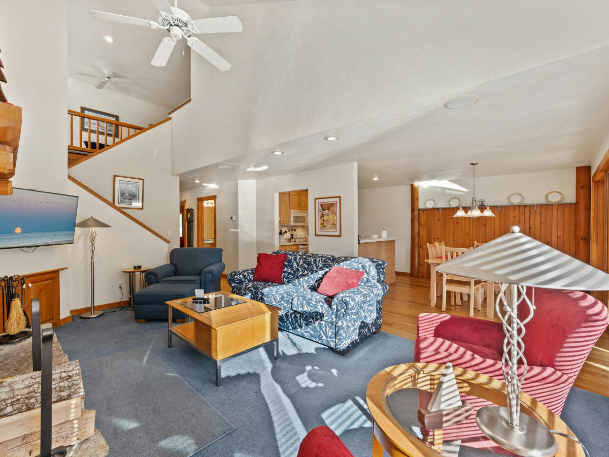 Bright living room with patterned sofas, armchairs, a fireplace, TV, coffee tables, and a view of the dining area and staircase&mdash;all in a spacious open-plan layout with wooden accents&mdash;showcases the elegance you can achieve through thoughtful basement remodeling Atlanta homeowners appreciate.