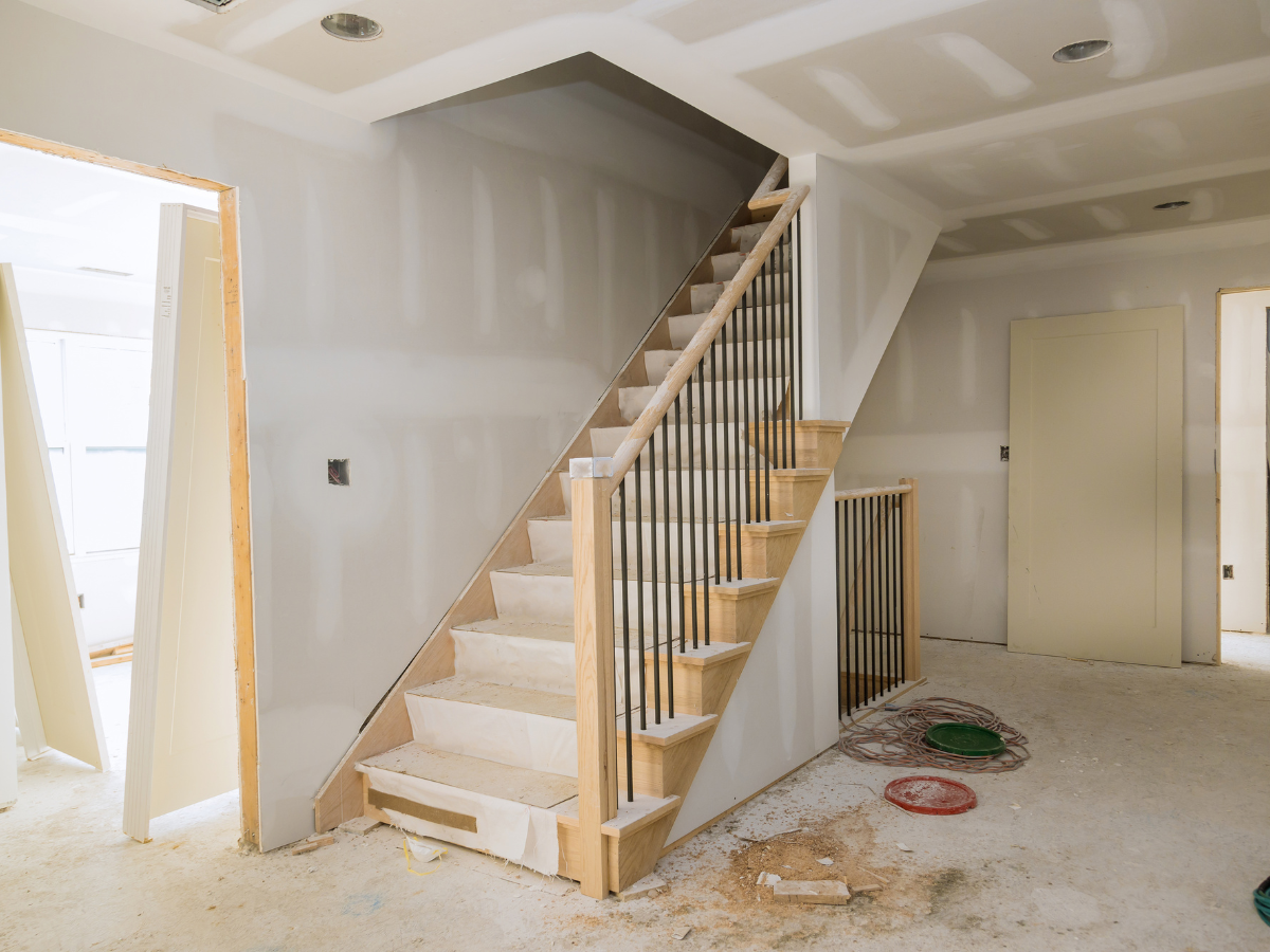 Unfinished interior with a staircase, drywall installed but unpainted&mdash;perfect for basement remodeling Atlanta projects&mdash;with construction materials and debris scattered on the floor.