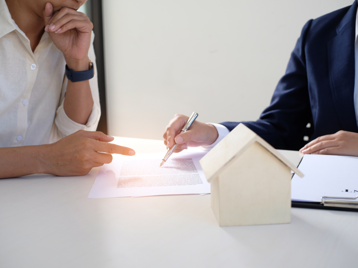 Insurance Claim Assistance For Property Damage Restoration 1 Two people review and sign paperwork at a desk with a small wooden house model, one person pointing at the document, as they receive insurance claim assistance.