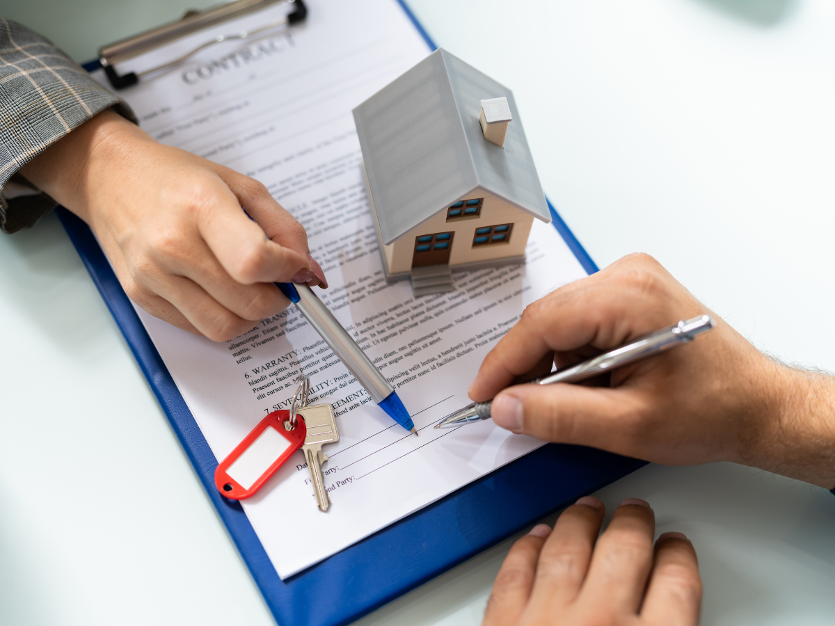 Insurance Claim Assistance For Property Damage Restoration 3 Two people review and sign a real estate contract with a small model house and keys on the document, symbolizing a property transaction and the importance of insurance claim assistance throughout the process.