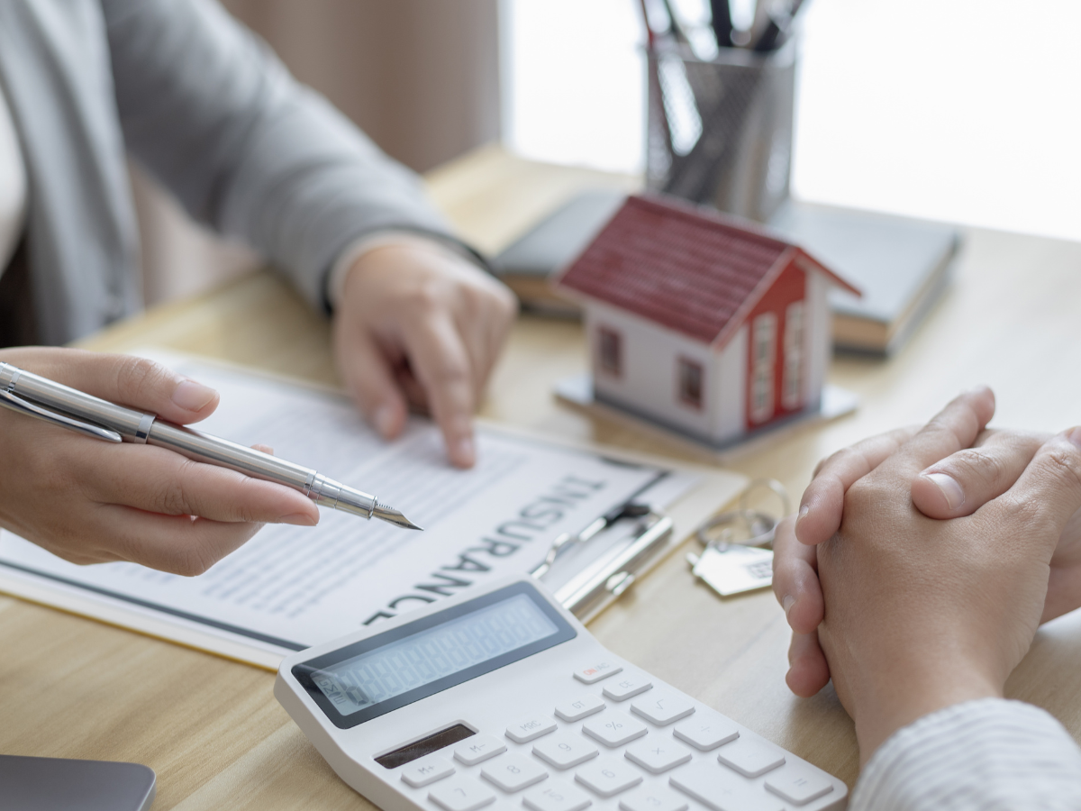 Insurance Claim Assistance For Property Damage Restoration 4 Two people discuss insurance paperwork at a desk with a calculator, model house, and keys in view, seeking insurance claim assistance.
