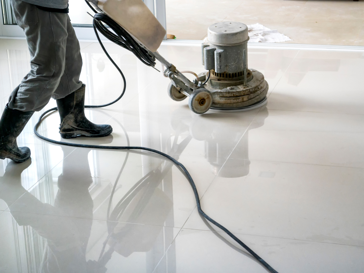 Floor Care Schedule For Cleaner, Longer-Lasting Floors 2 Person wearing boots operates a floor polishing machine on a shiny tile floor, with the power cord visible on the ground—highlighting the importance of a regular floor care schedule for maintaining spotless surfaces.
