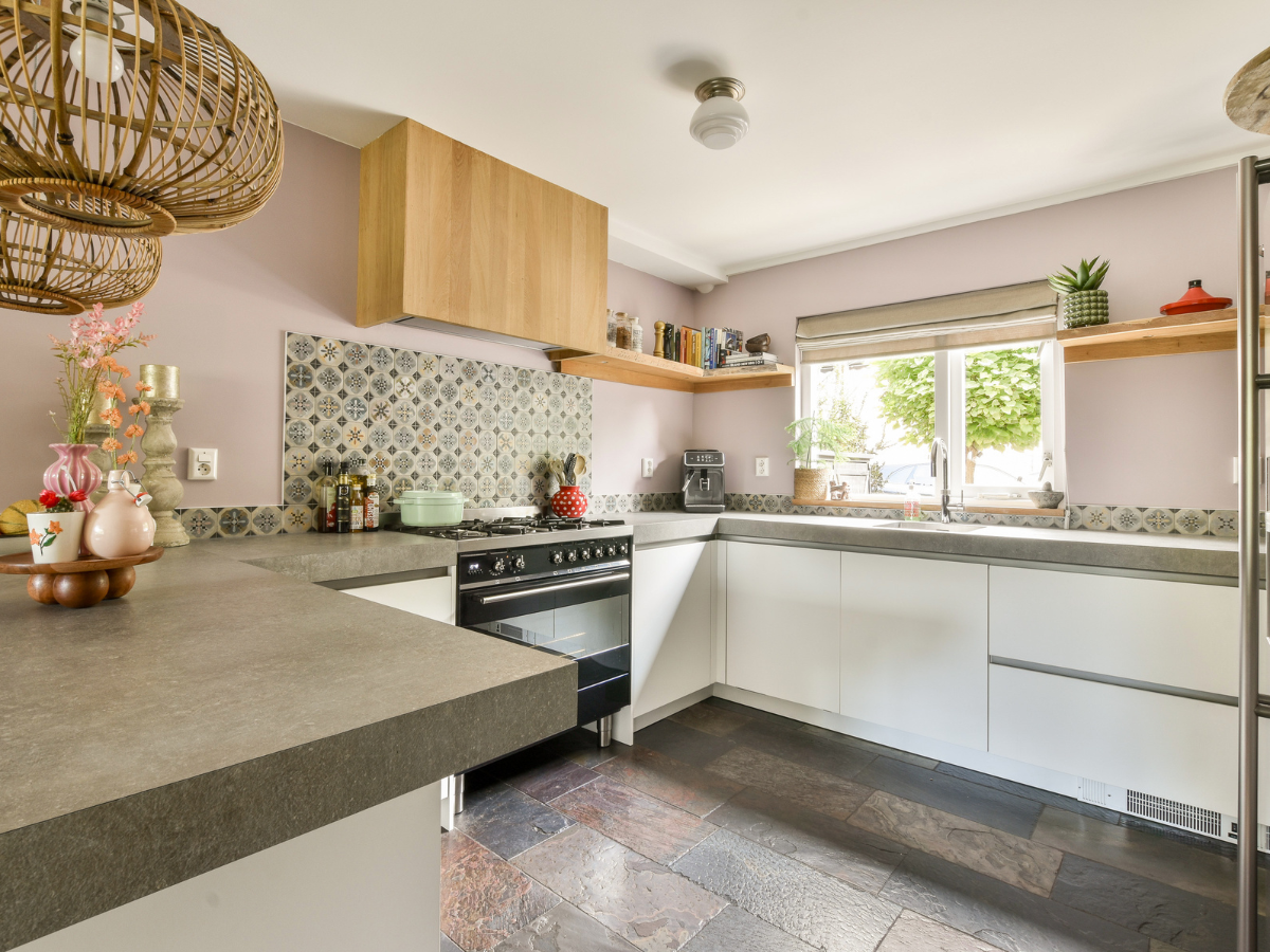 Modern kitchen with white cabinets, stone countertops, patterned tile backsplash, stove, window with blind, and decorative items on shelves and countertop&mdash;a perfect setting for those considering tile vs hardwood in their design choices.